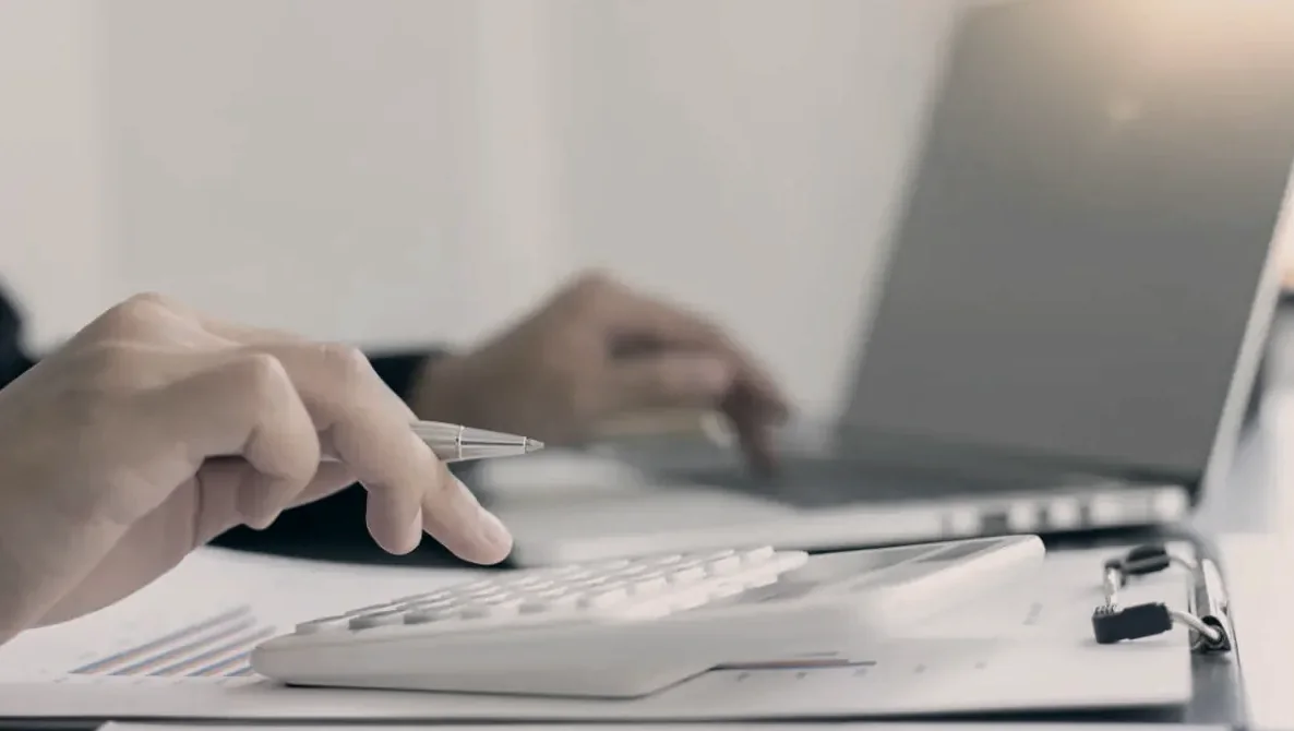 Mãos calculando valores em calculadora e notebook, simulação de regras de aposentadoria