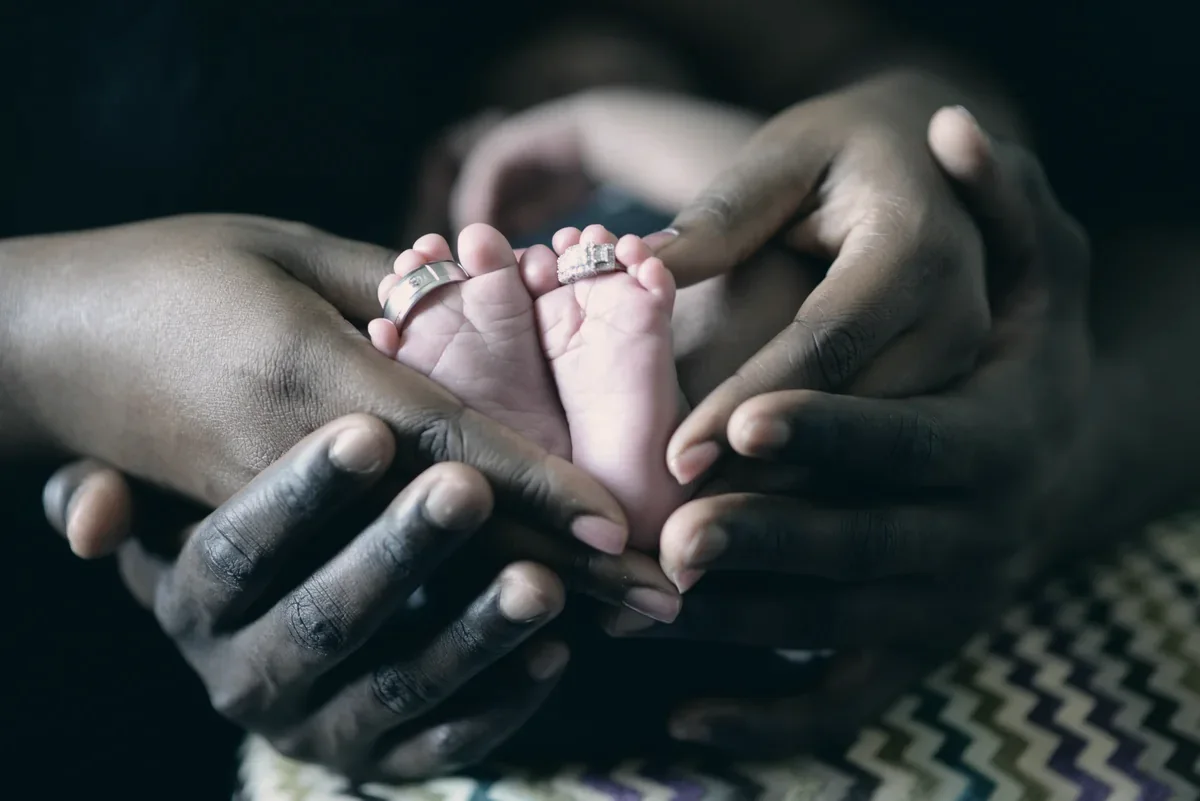 Mãos de familiares segurando os pés de um recém-nascido
